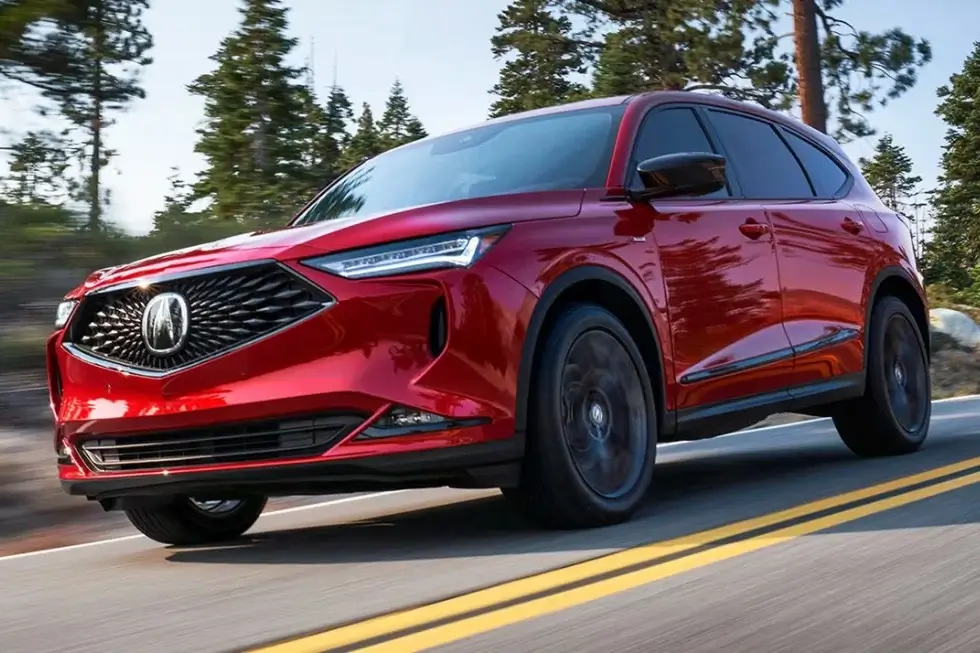 A red Acura MDX SUV driving down a road with trees in the background